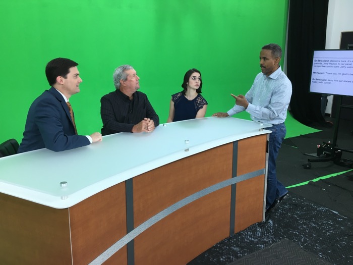 Ken Frieson directing three show hosts at a desk in front of a green screen.